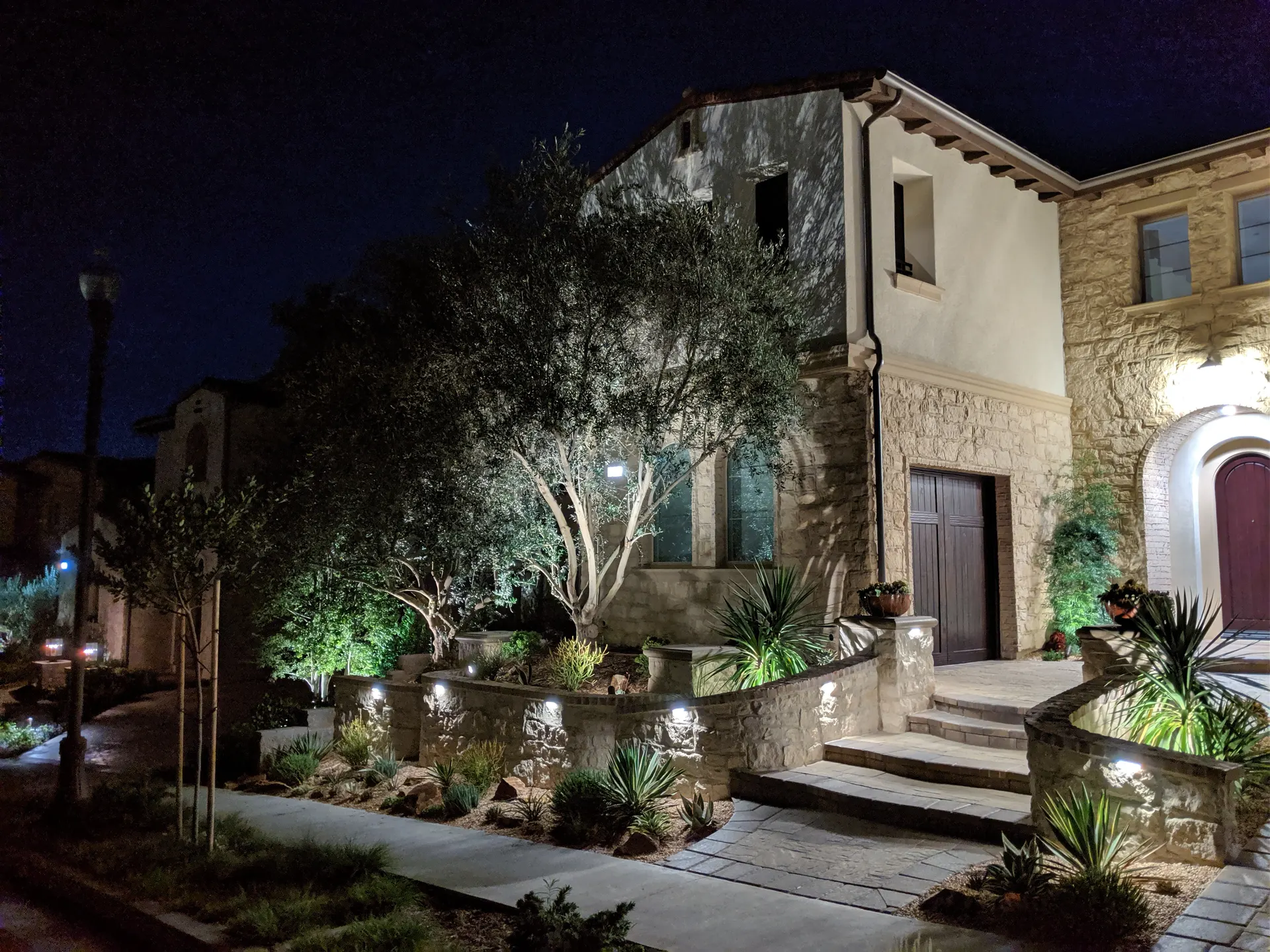 Night Mediterranean home with tree uplighting and lit stone planters