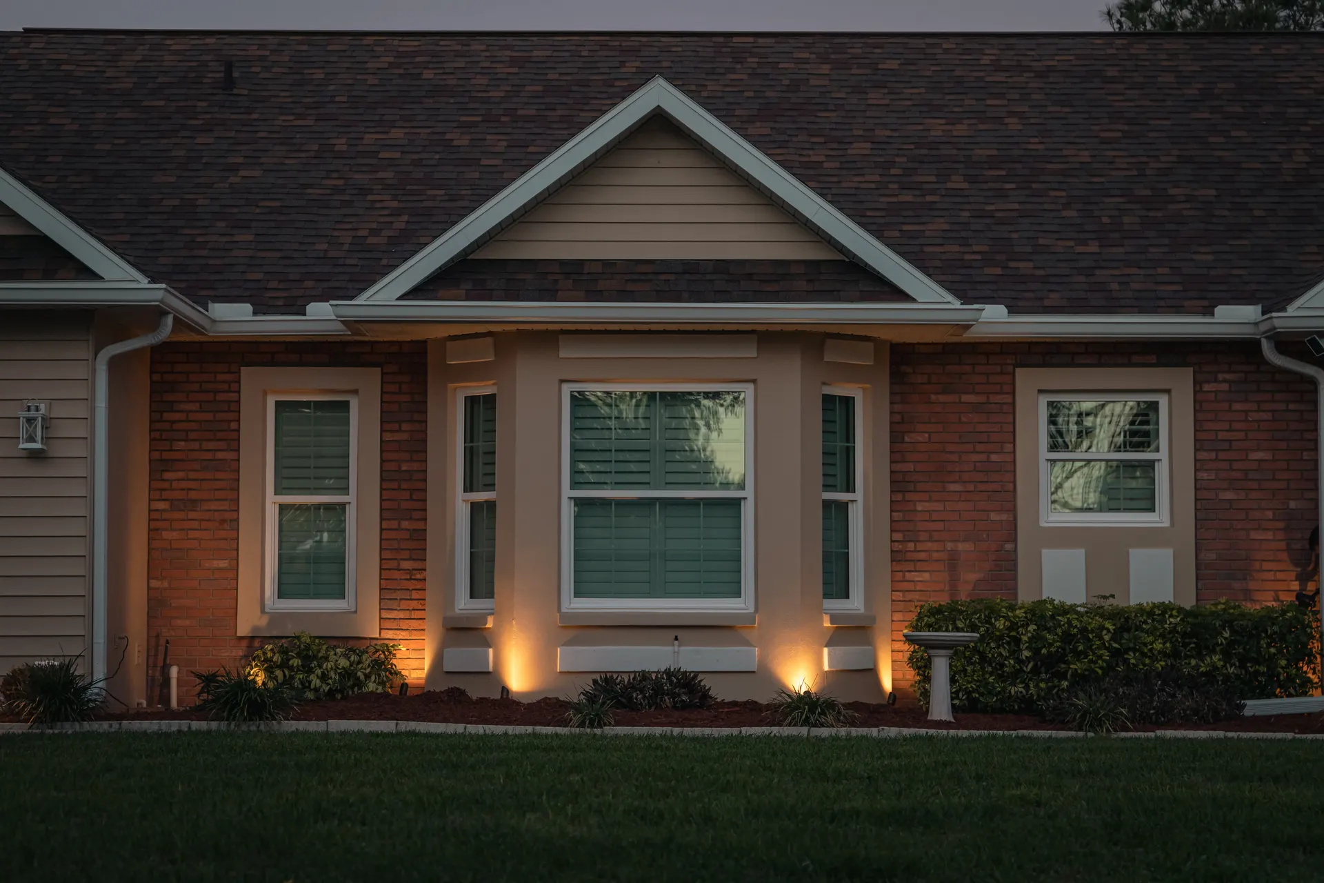 Brick home with warm uplit columns and windows at dusk, balanced