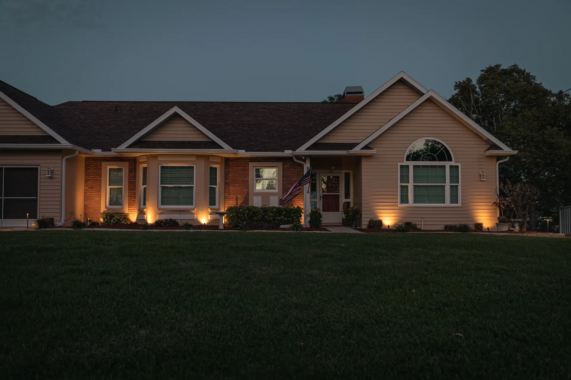 Ranch home at dusk with even warm facade uplighting, clean composition