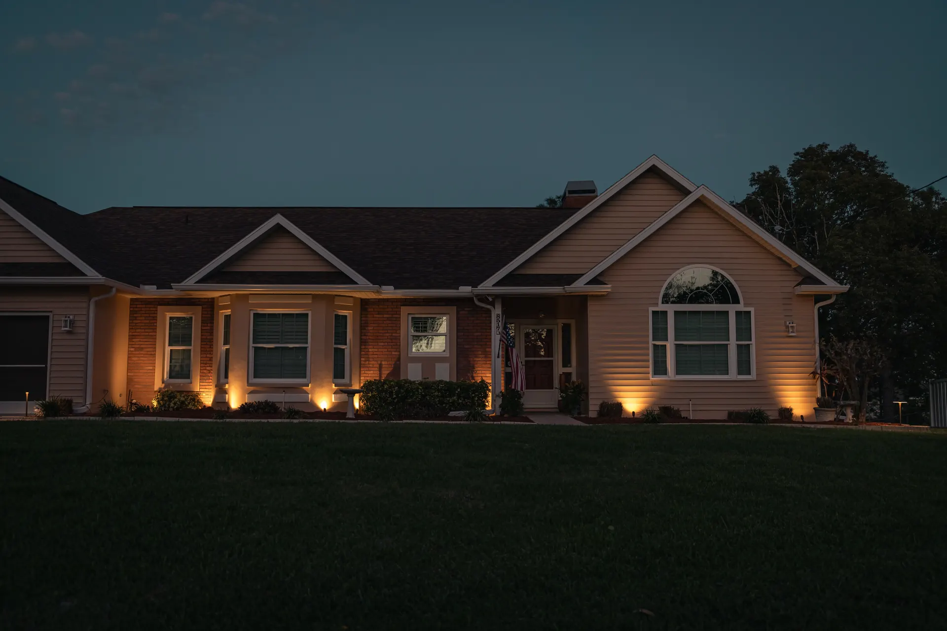 Home at twilight with warm column and facade uplights, rich blue sky