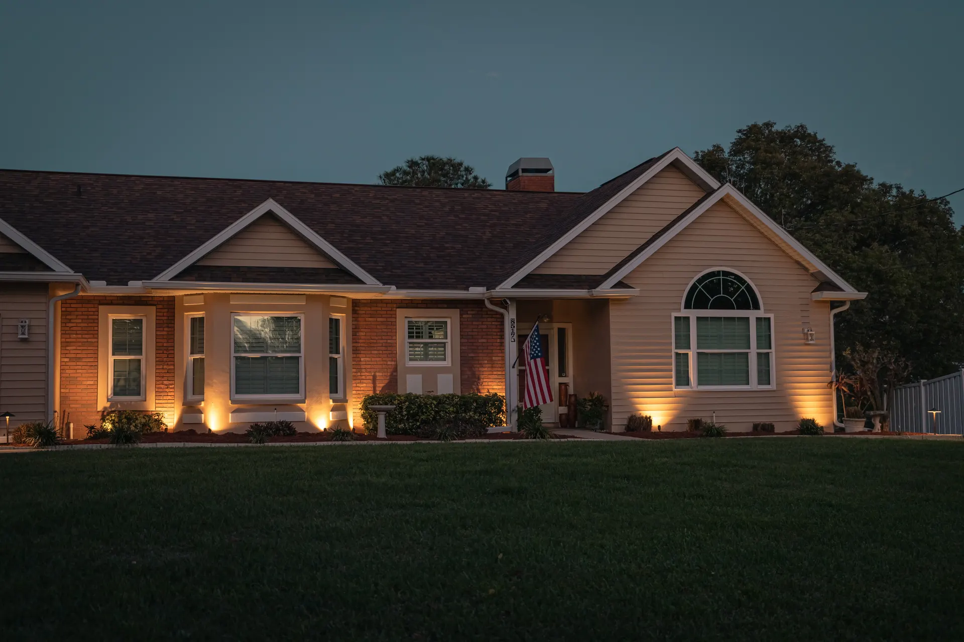 Home at dusk with warm porch and gable uplights, deep sky, strong scene