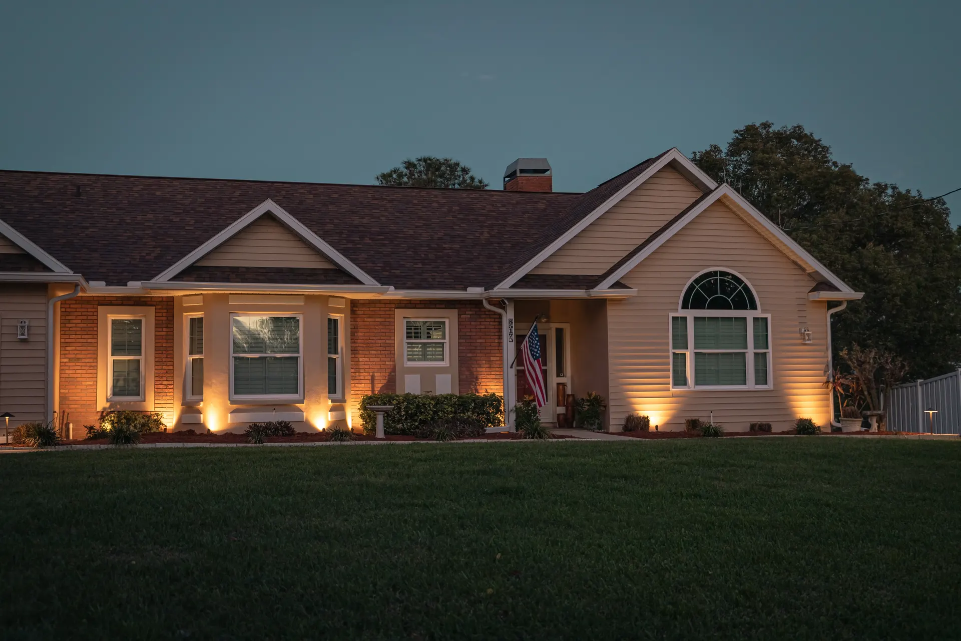 Brick home at twilight, warm uplights on columns and gable