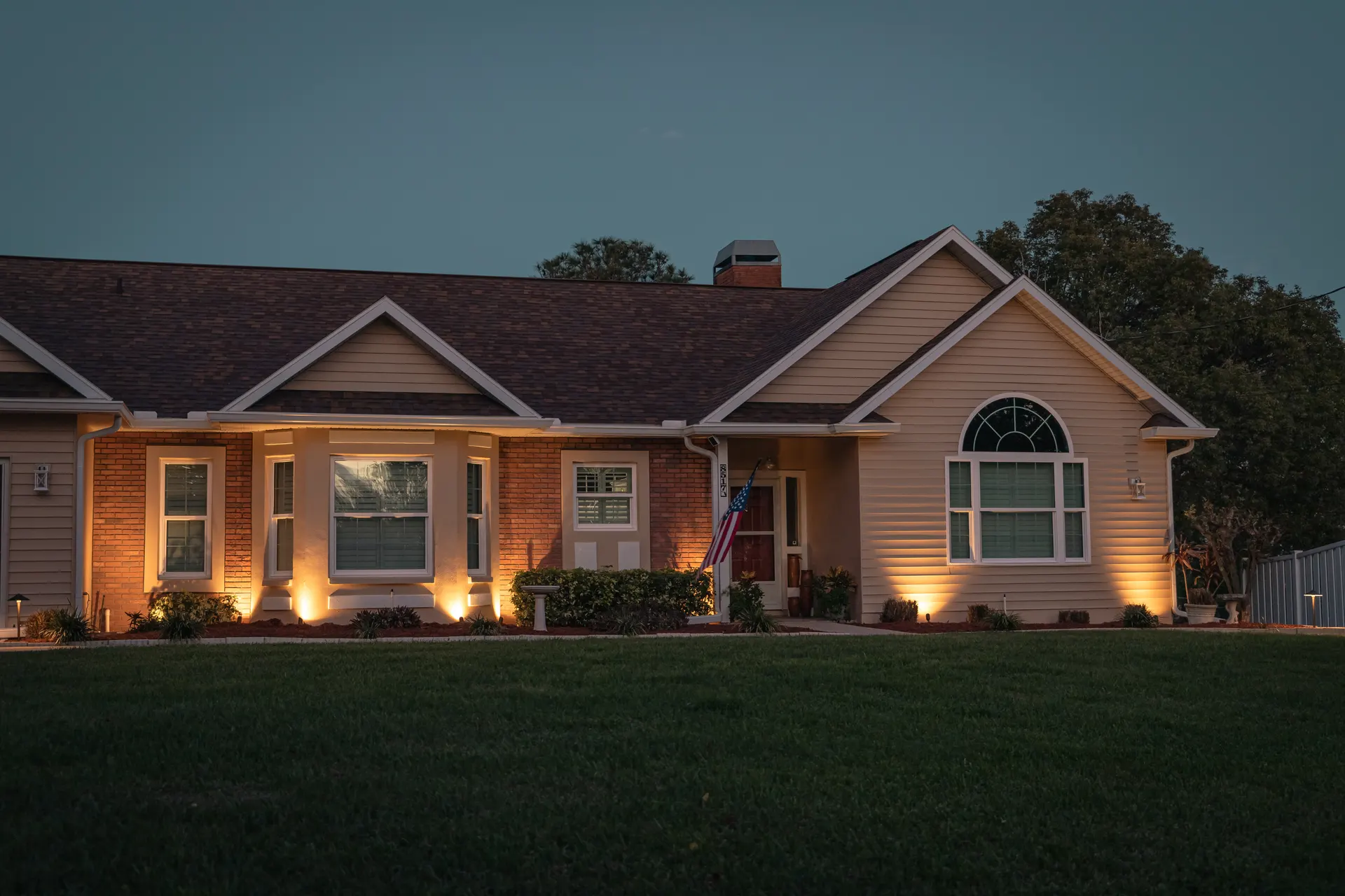 Home at dusk with warm facade and porch uplights, blue sky, inviting