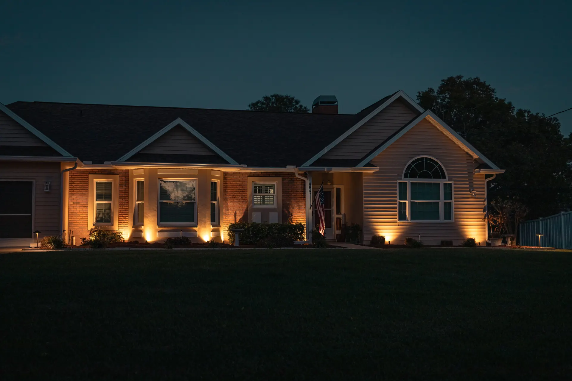 Dusk ranch home, warm uplighting on brick facade and entry, lit windows