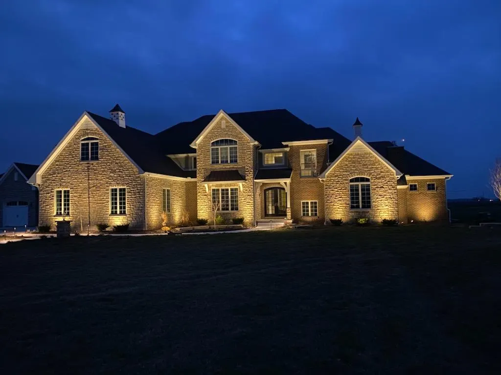 Dusk stone mansion, warm facade uplighting across full front, lit entry