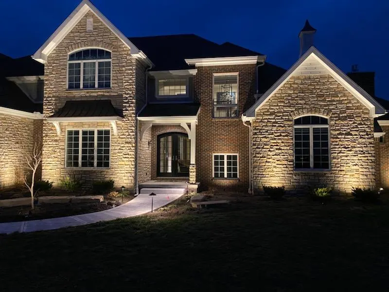 Night brick-stone home, even warm uplighting on facade, lit walkway