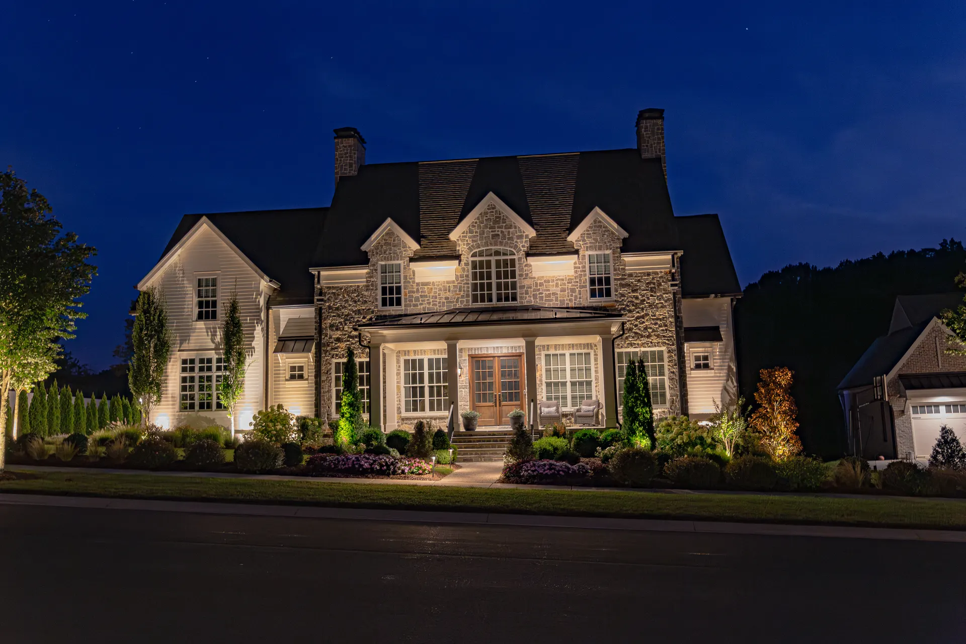 Dusk stone home, warm facade and landscape lighting, deep blue sky