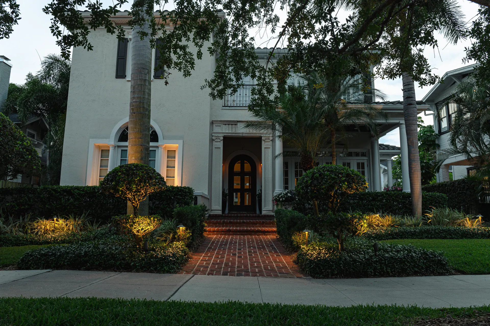 Two-story white home, lit walkway and uplit shrubs, polished dusk curb appeal