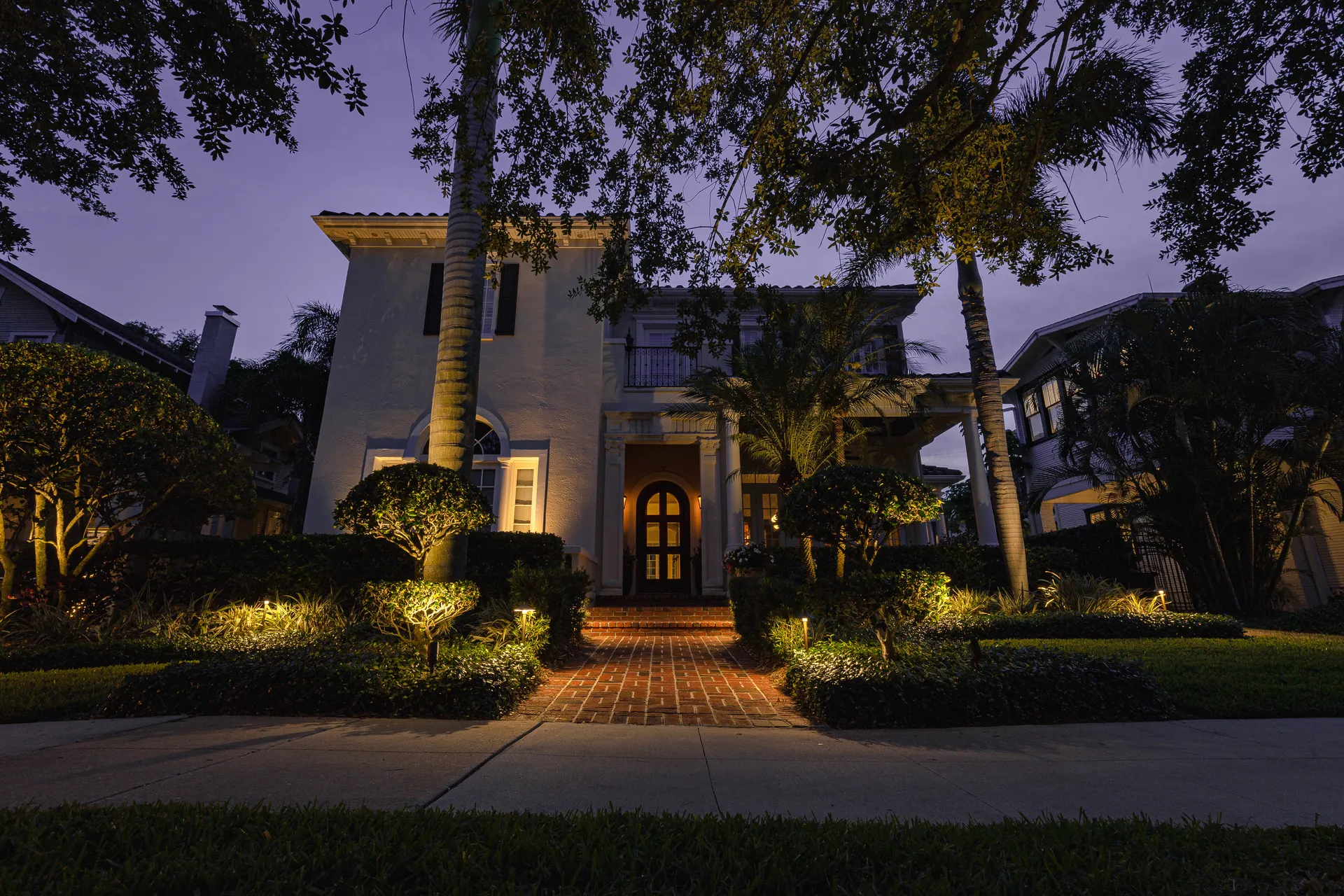 Mediterranean home at dusk, uplit palms, glowing entry, purple sky