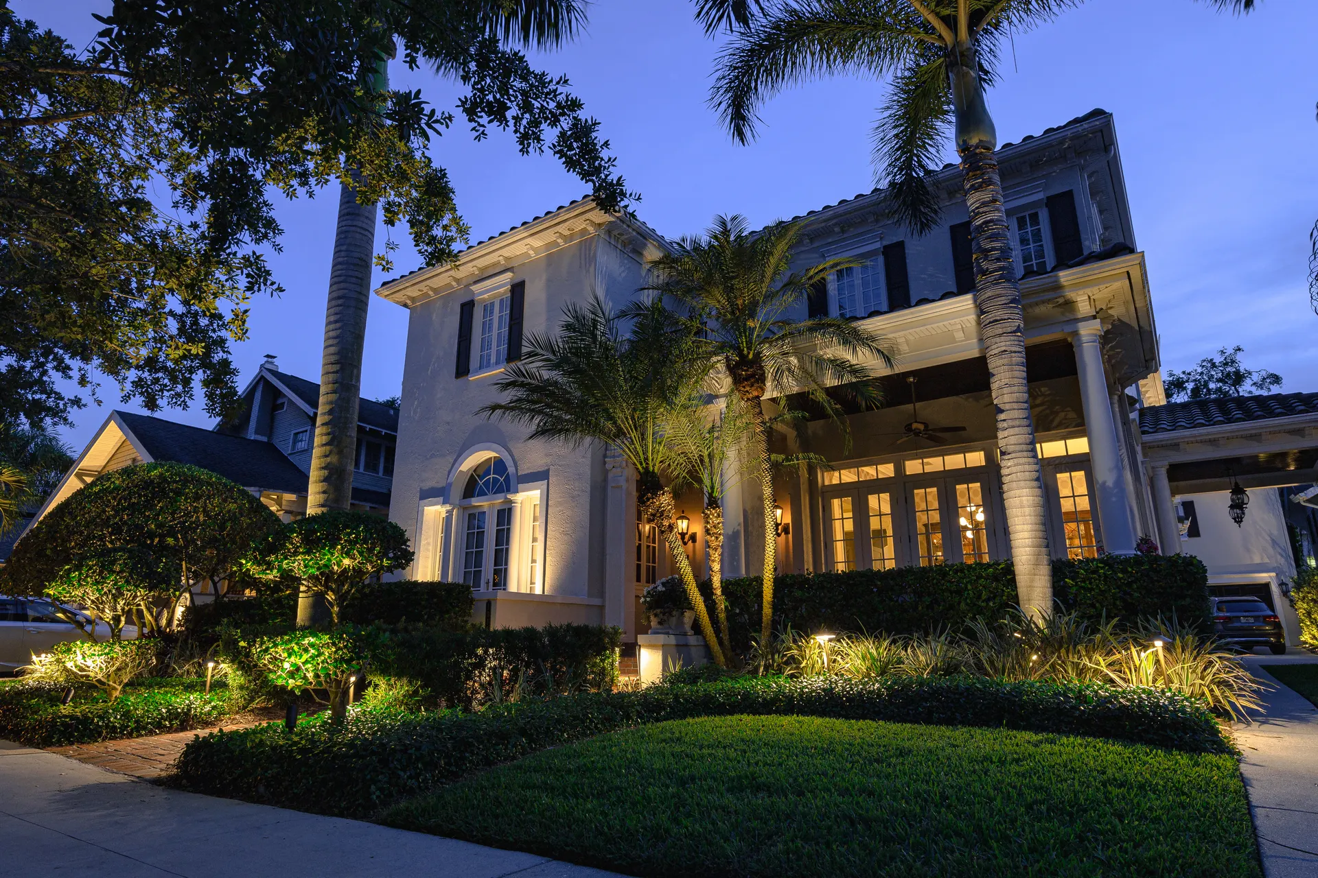 Elegant home dusk, uplit palms and hedges, warm glowing windows