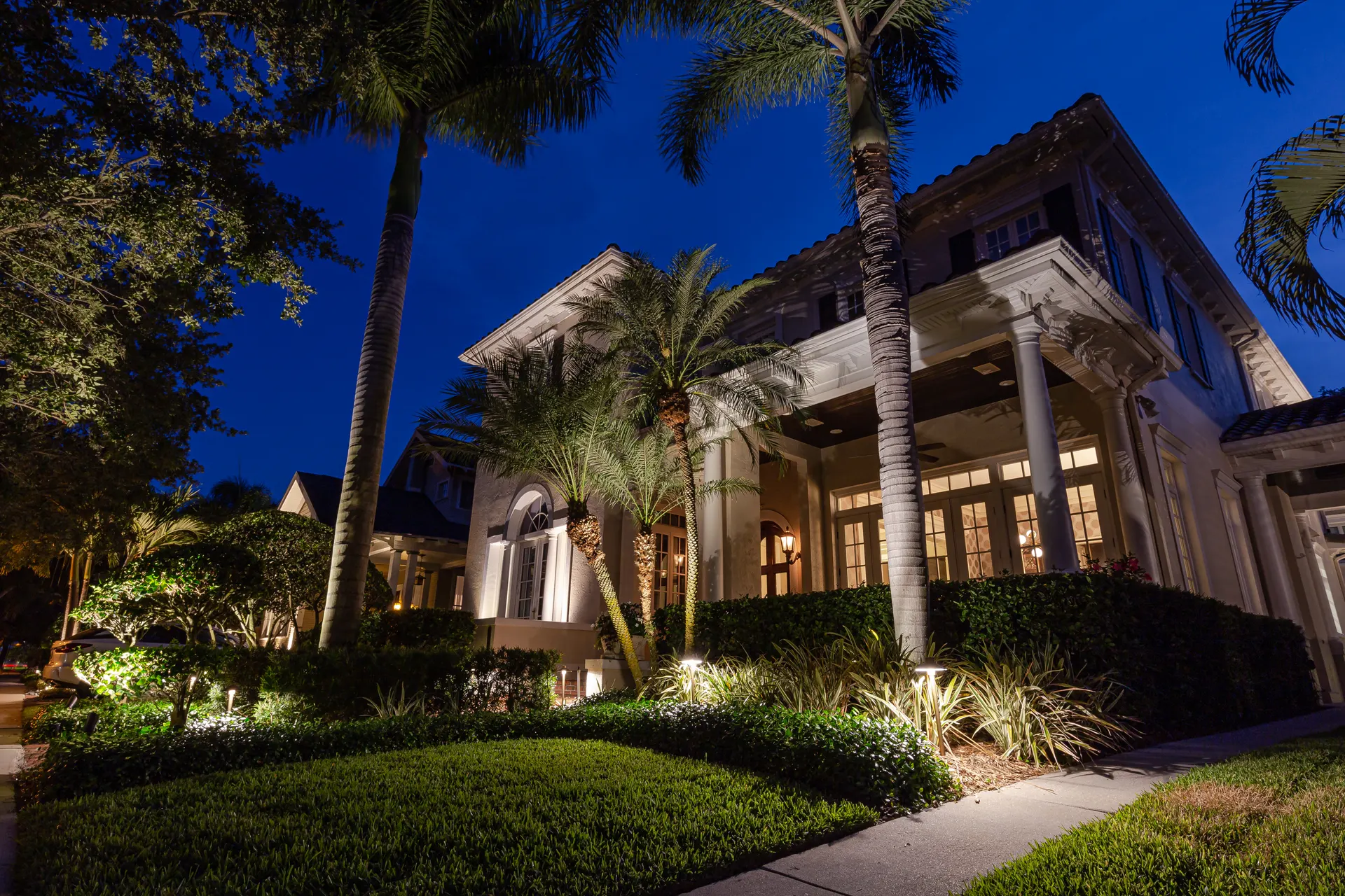 Grand home at blue dusk, uplit palms and entry columns, warm glow