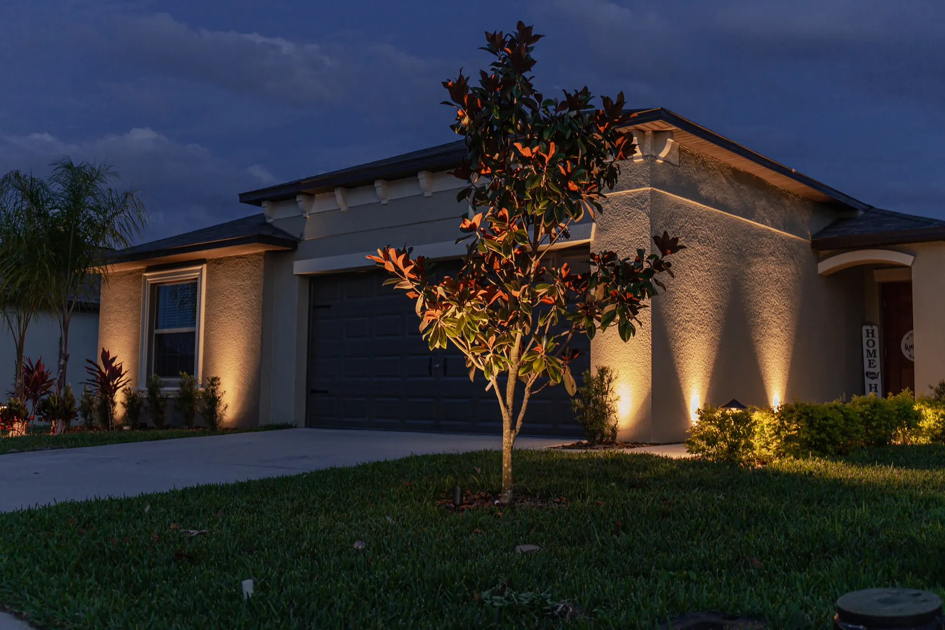 Single-story home, symmetrical warm uplights on facade and tree, clean dusk