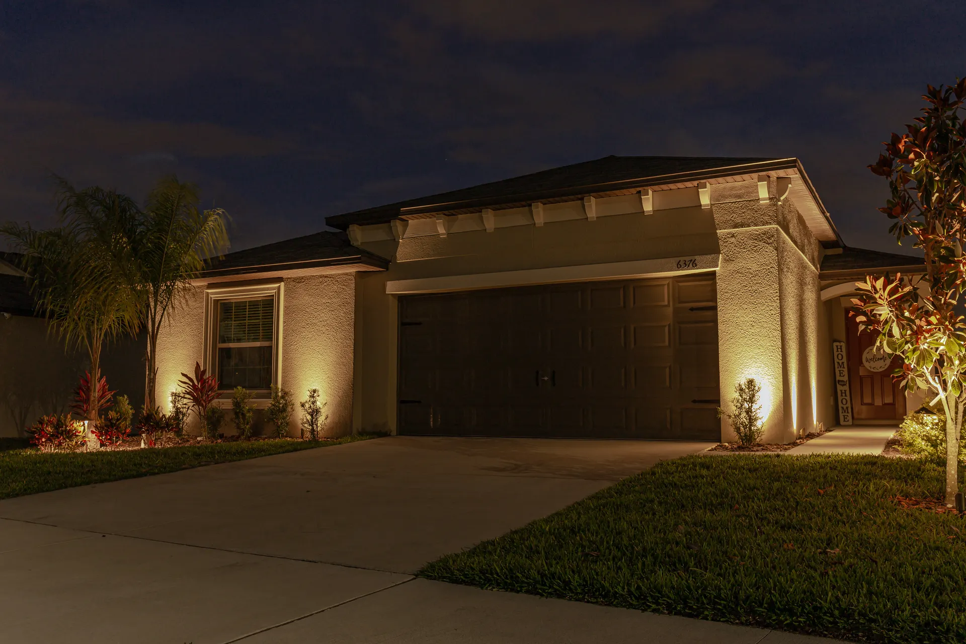 One-story home at night, uplit palms and entry, warm balanced facade lighting