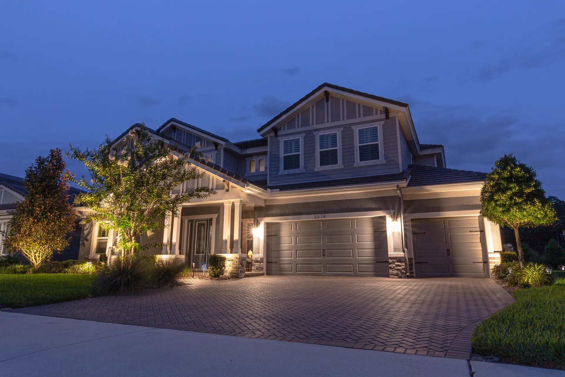Gray craftsman home at dusk, uplit trees flanking entry, warm balanced glow
