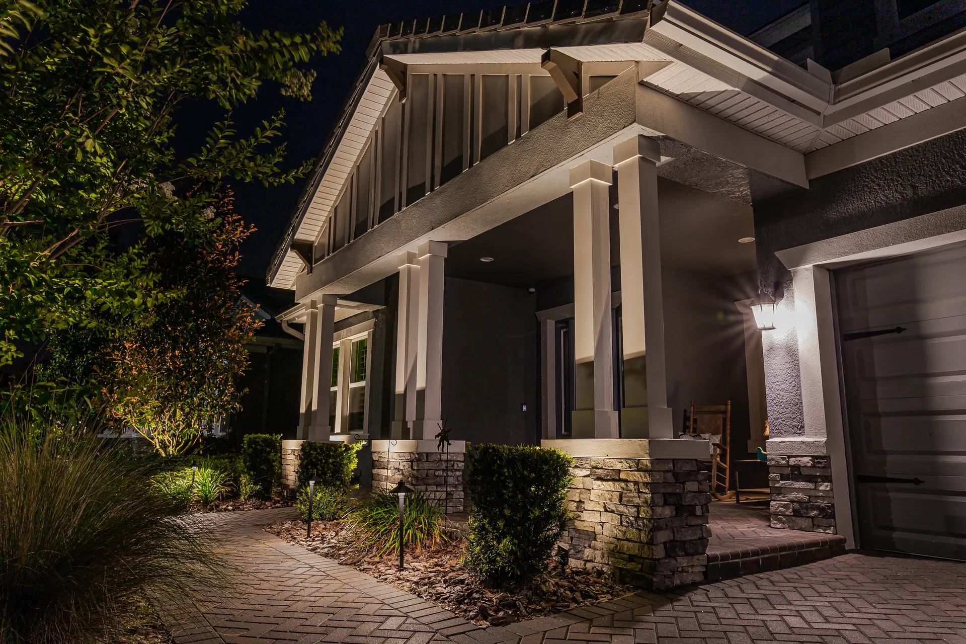 Craftsman porch columns lit, uplit shrubs and tree, paver walkway detail