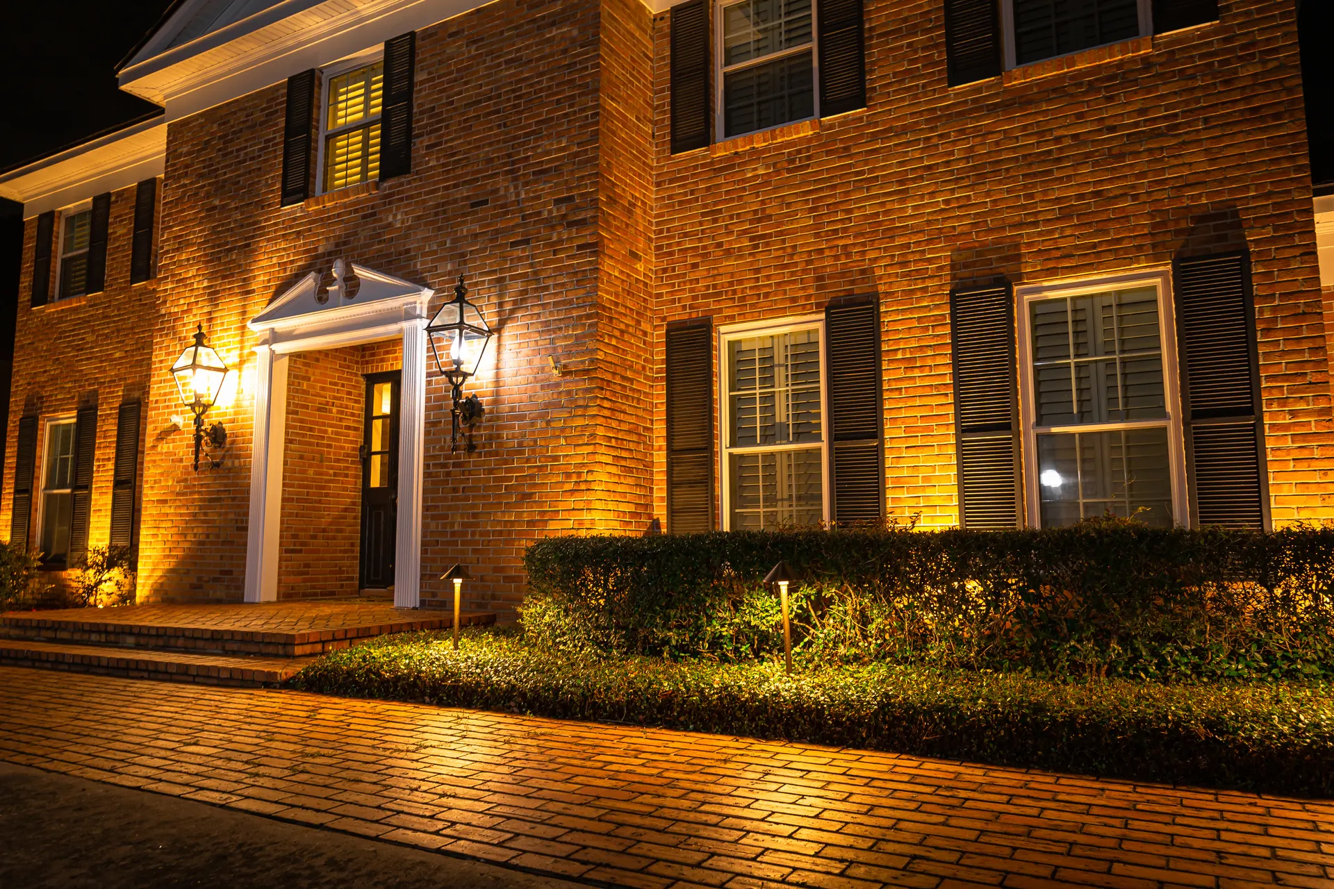 Brick colonial warm uplighting, lit entry, paver driveway, polished night shot