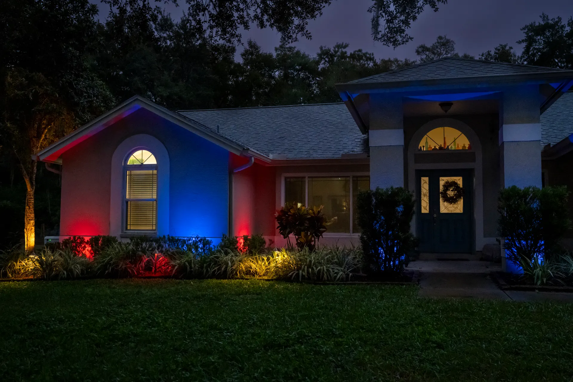 Single-story home patriotic red-white-blue facade wash, lit entry, dusk