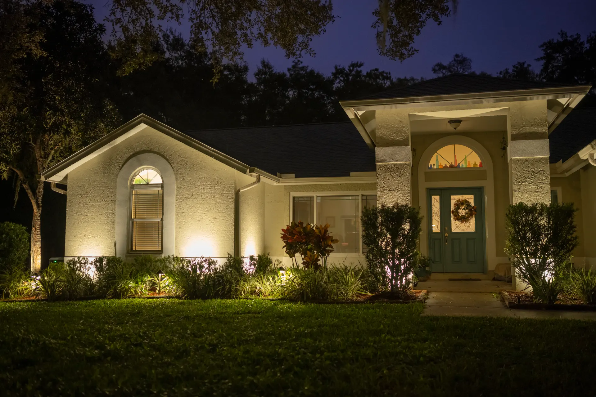 White brick home warm facade uplighting, lit entry arch, deep blue dusk