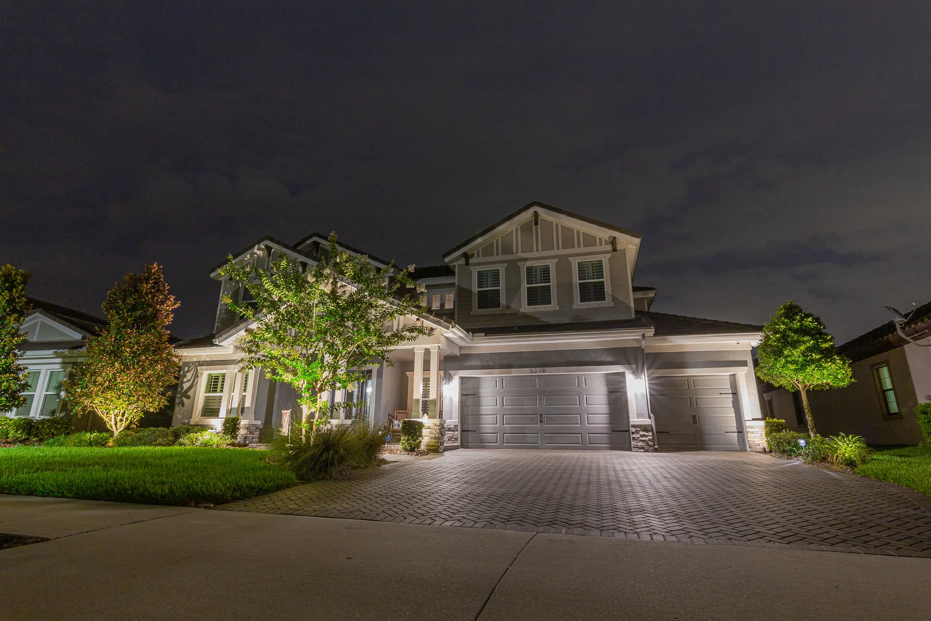 Two-story home night, even facade lighting, uplit trees, dramatic sky