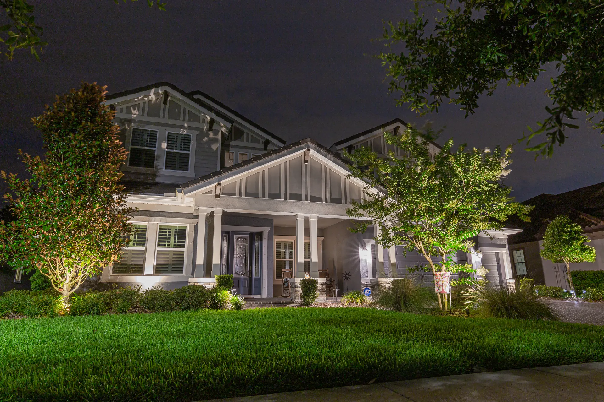 Craftsman porch night, gable and columns lit, uplit trees, manicured lawn