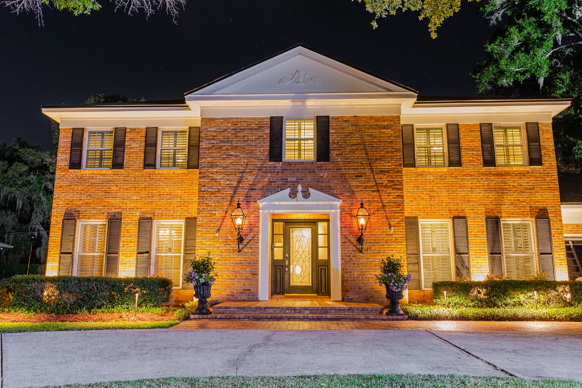 Colonial home night, warm-white facade wash, lit entry urns and columns