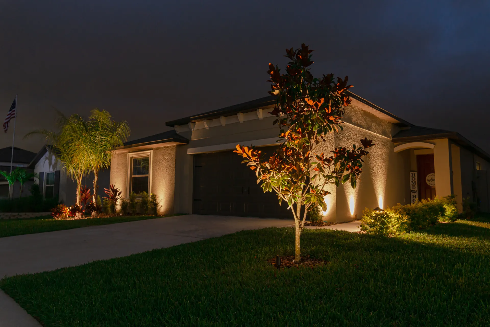 Single-story home night, facade wash and tree uplighting, warm and inviting