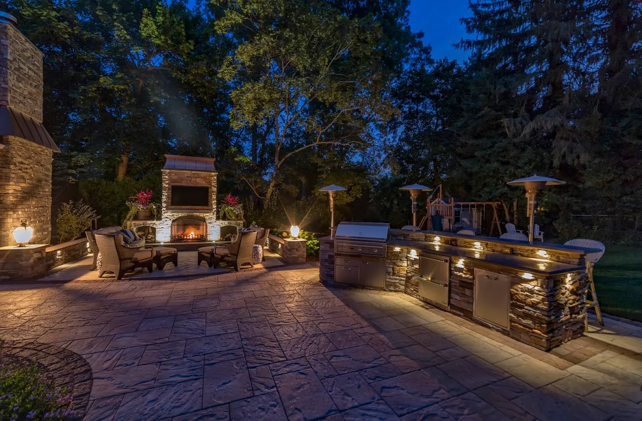 Dusk outdoor kitchen and stone fireplace, warm lit patio living space