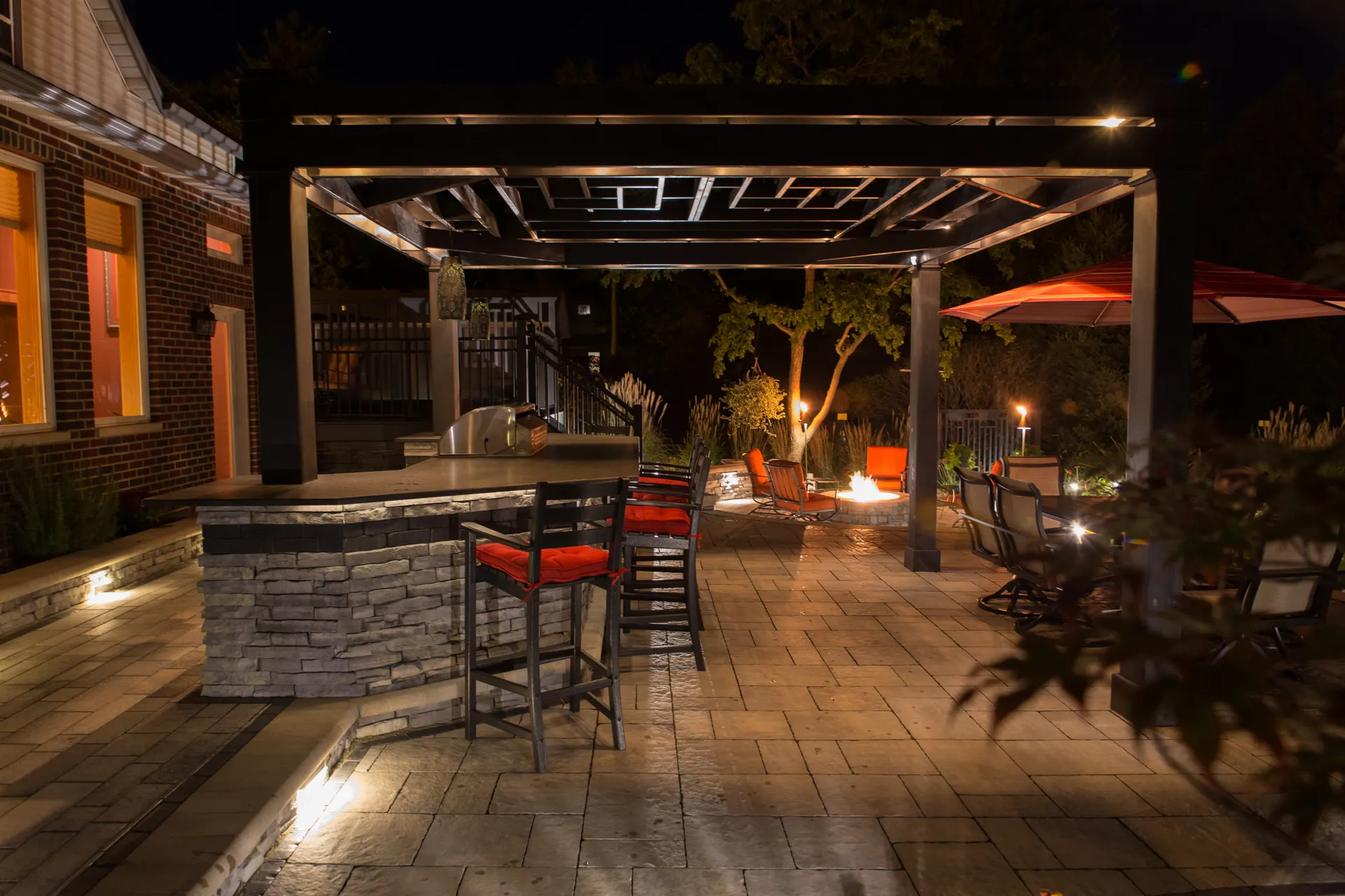 Night pergola patio with bar, uplit posts, fire pit, warm glow