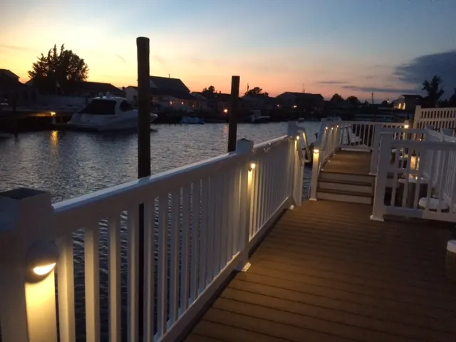 Waterfront deck at sunset, warm rail lights, boats, marina, inviting glow