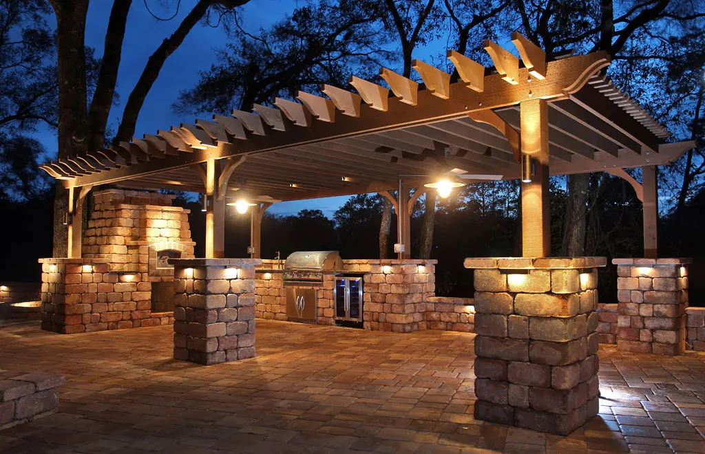 Outdoor kitchen pergola, stone columns with cap lights, grill, dusk sky
