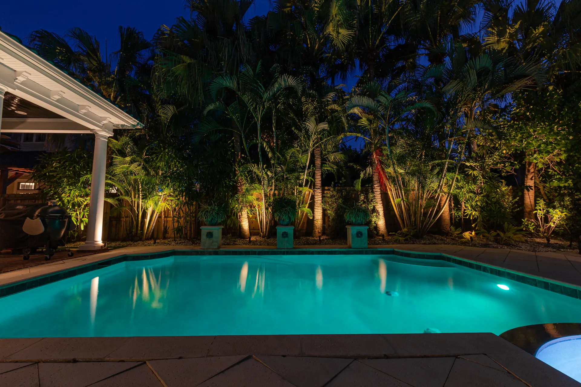 Lit turquoise pool framed by uplit palms, glowing cabana, tropical night scene