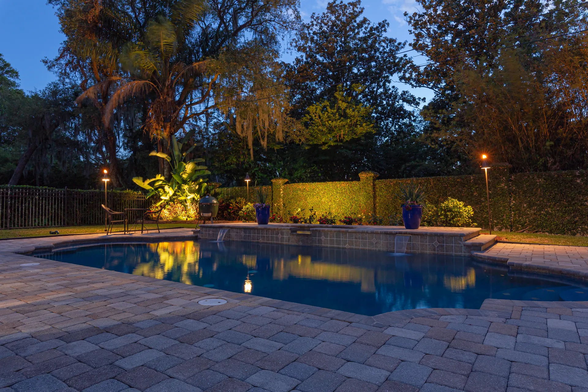 Dusk pool with reflections, lit path bollards, uplit palms, paver deck