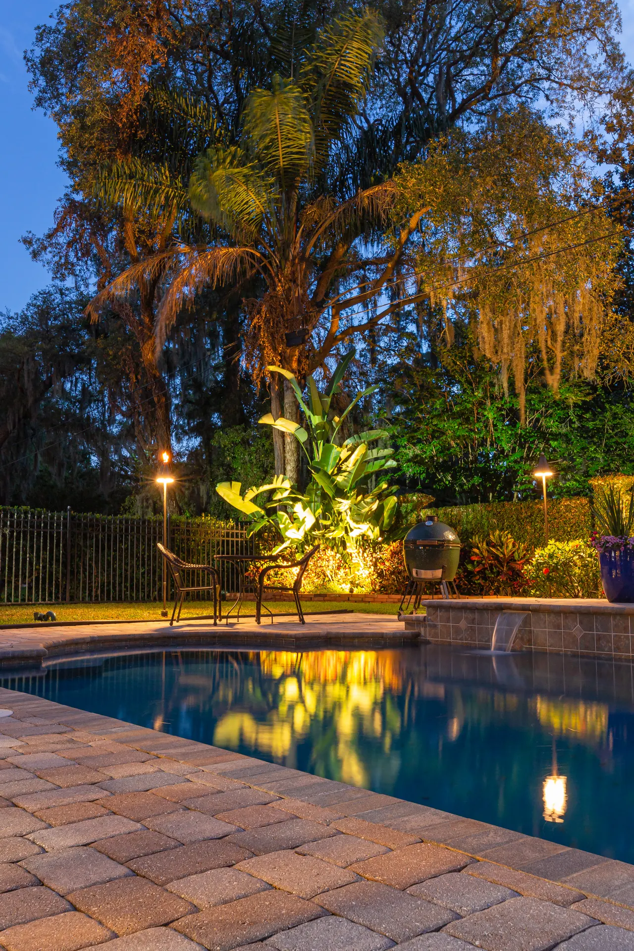 Dusk pool, uplit palm reflected, lit bollards, paver deck, portrait
