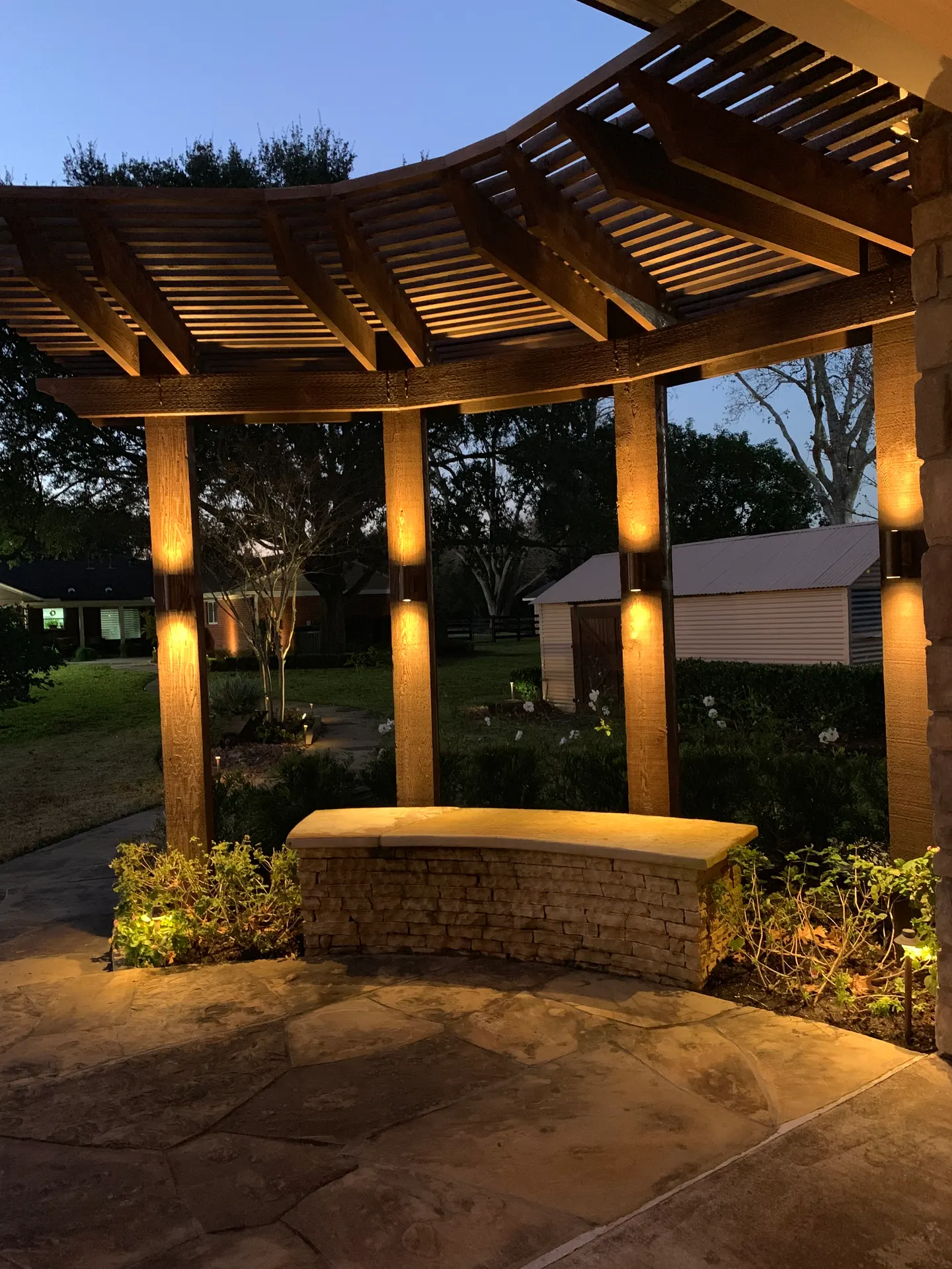 Dusk pergola with warm column uplighting and stone bench, garden