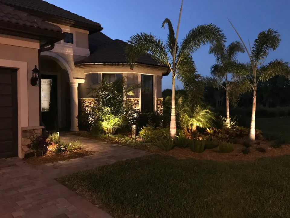 Dusk Florida home entry with palm and landscape uplighting, paver walk
