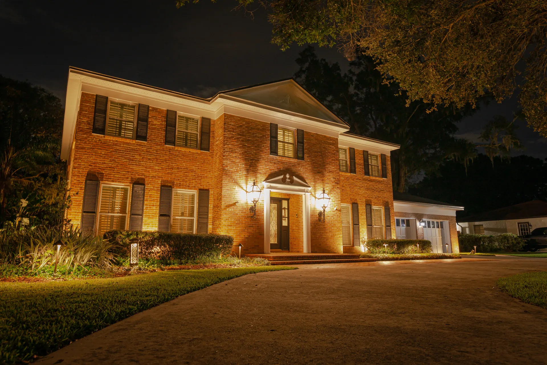 Brick colonial warm-white uplighting, lit entry sconces, clean night shot