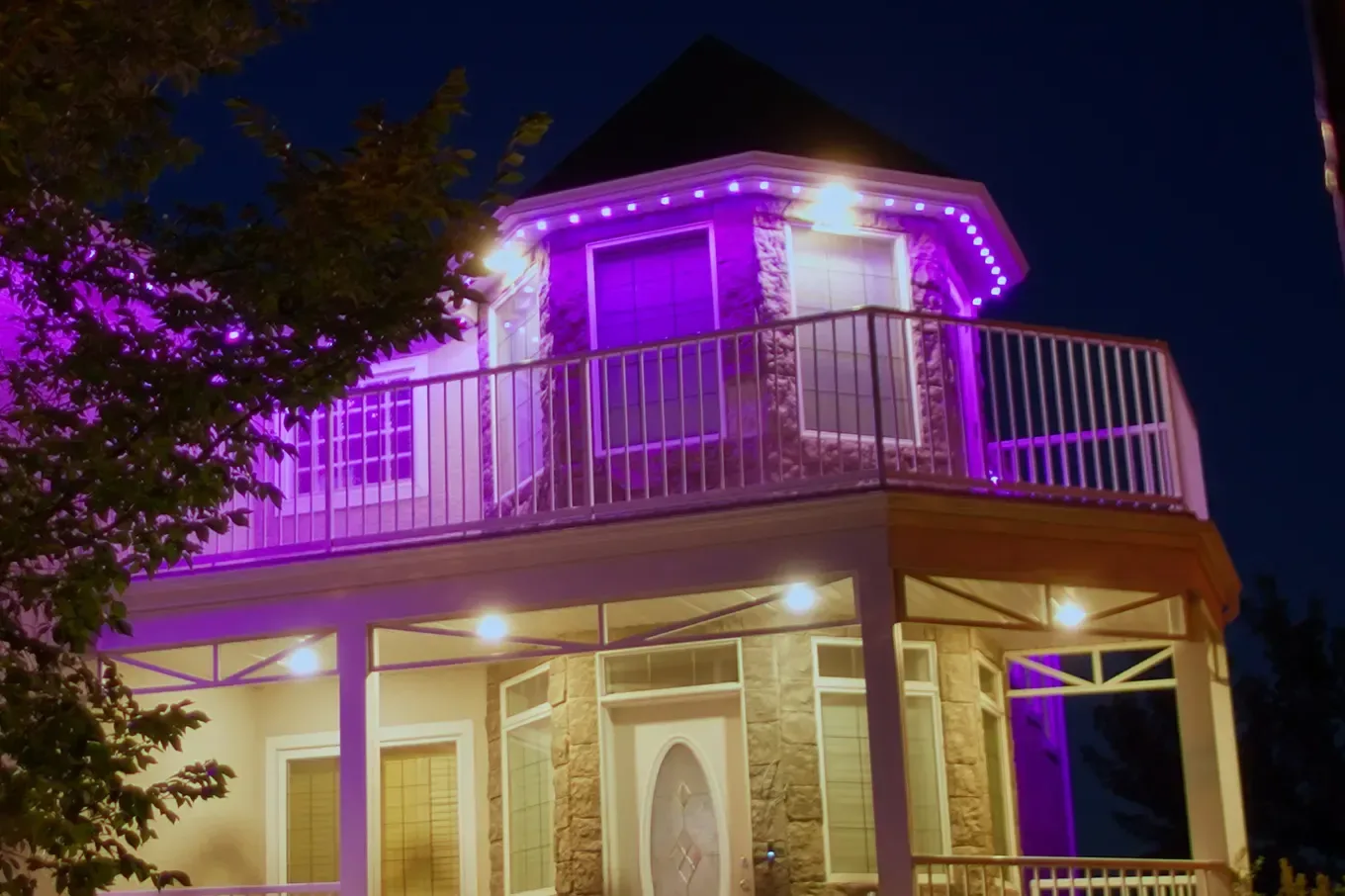 Two-story home with permanent lights in purple along the turret roofline and a purple wash on the walls at night