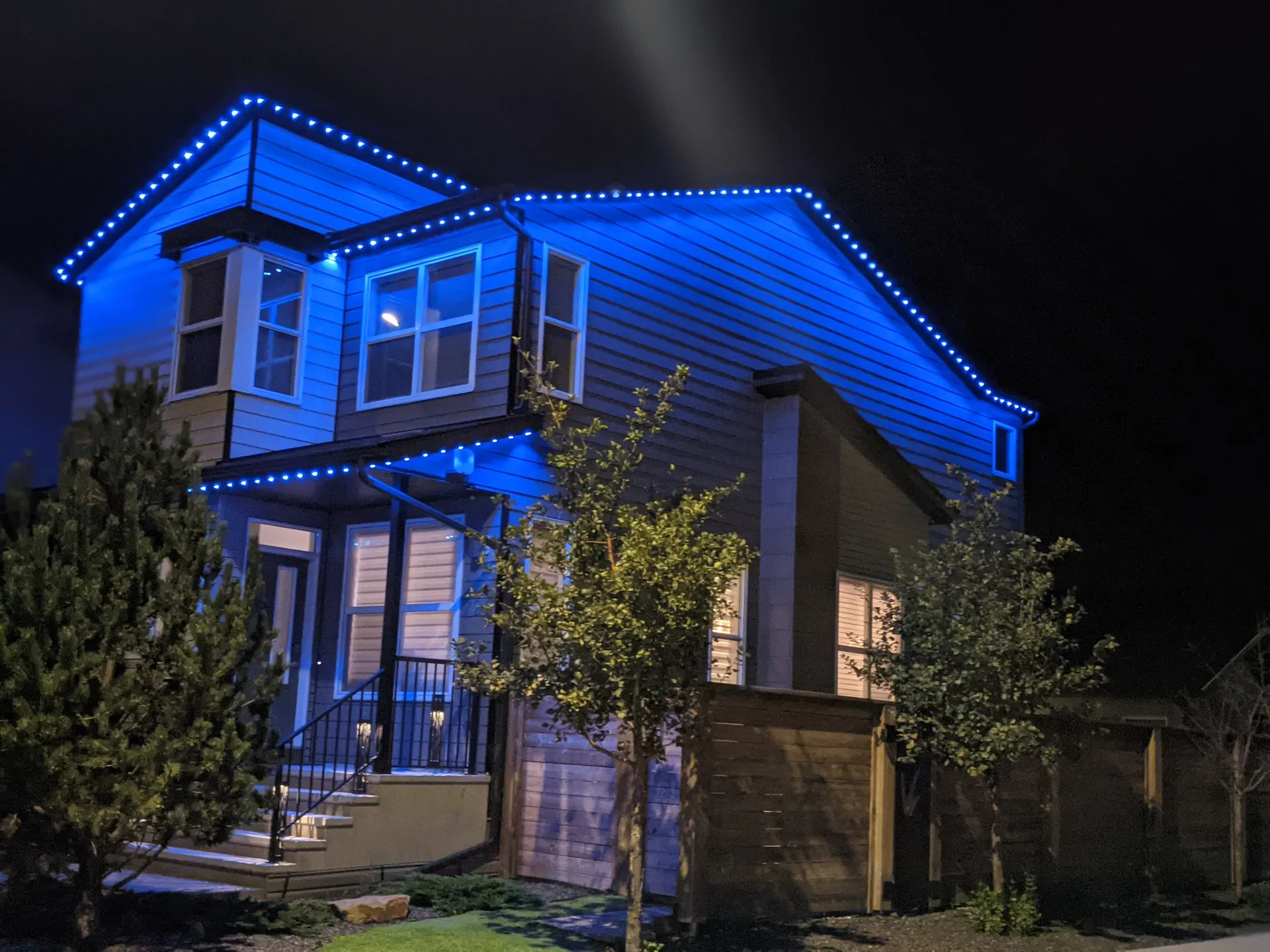 Two-story home rooflines and eaves outlined in vivid blue permanent lighting at night
