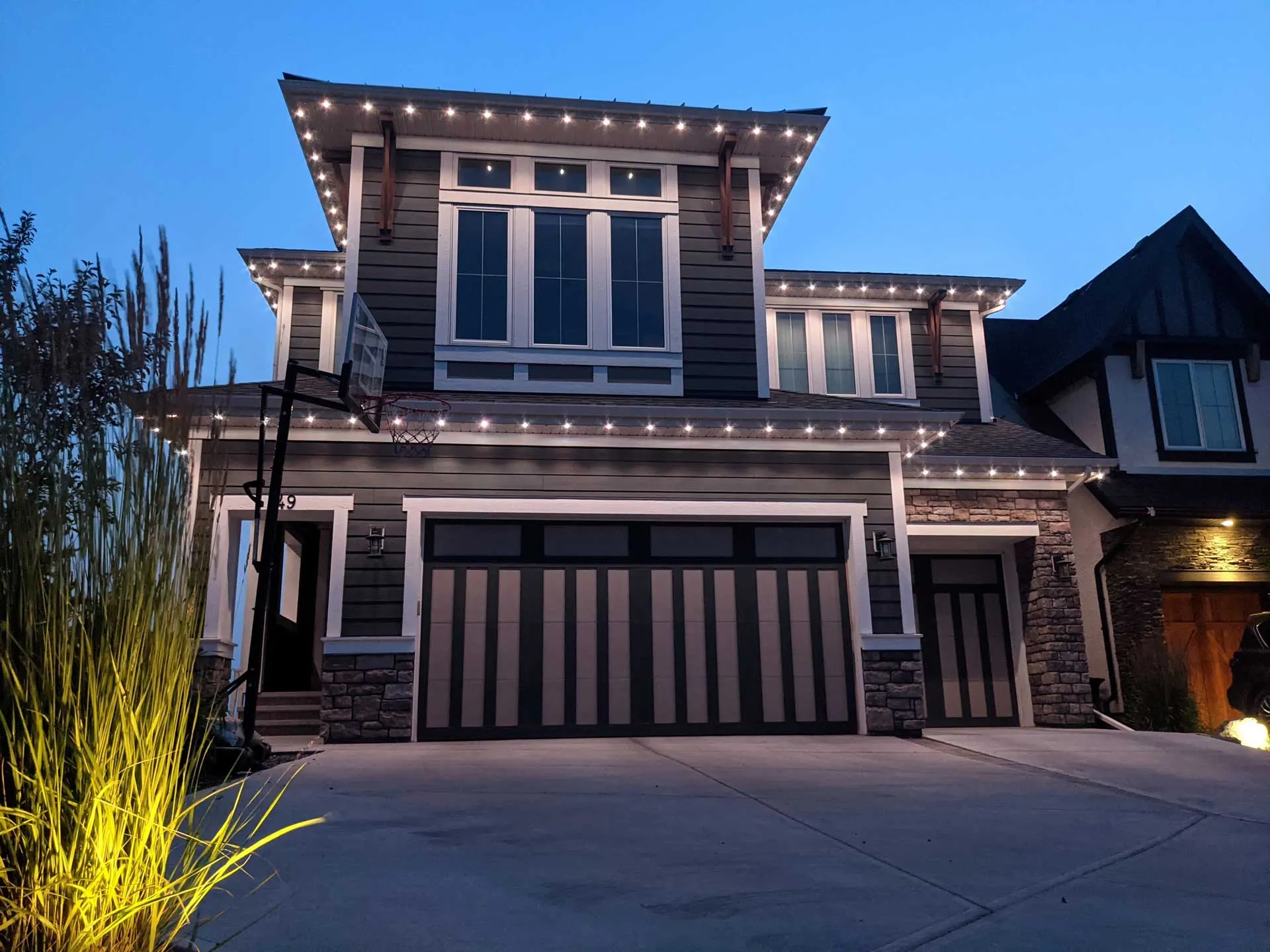 Modern home outlined warm white, eaves peaks garage, basketball hoop, dusk