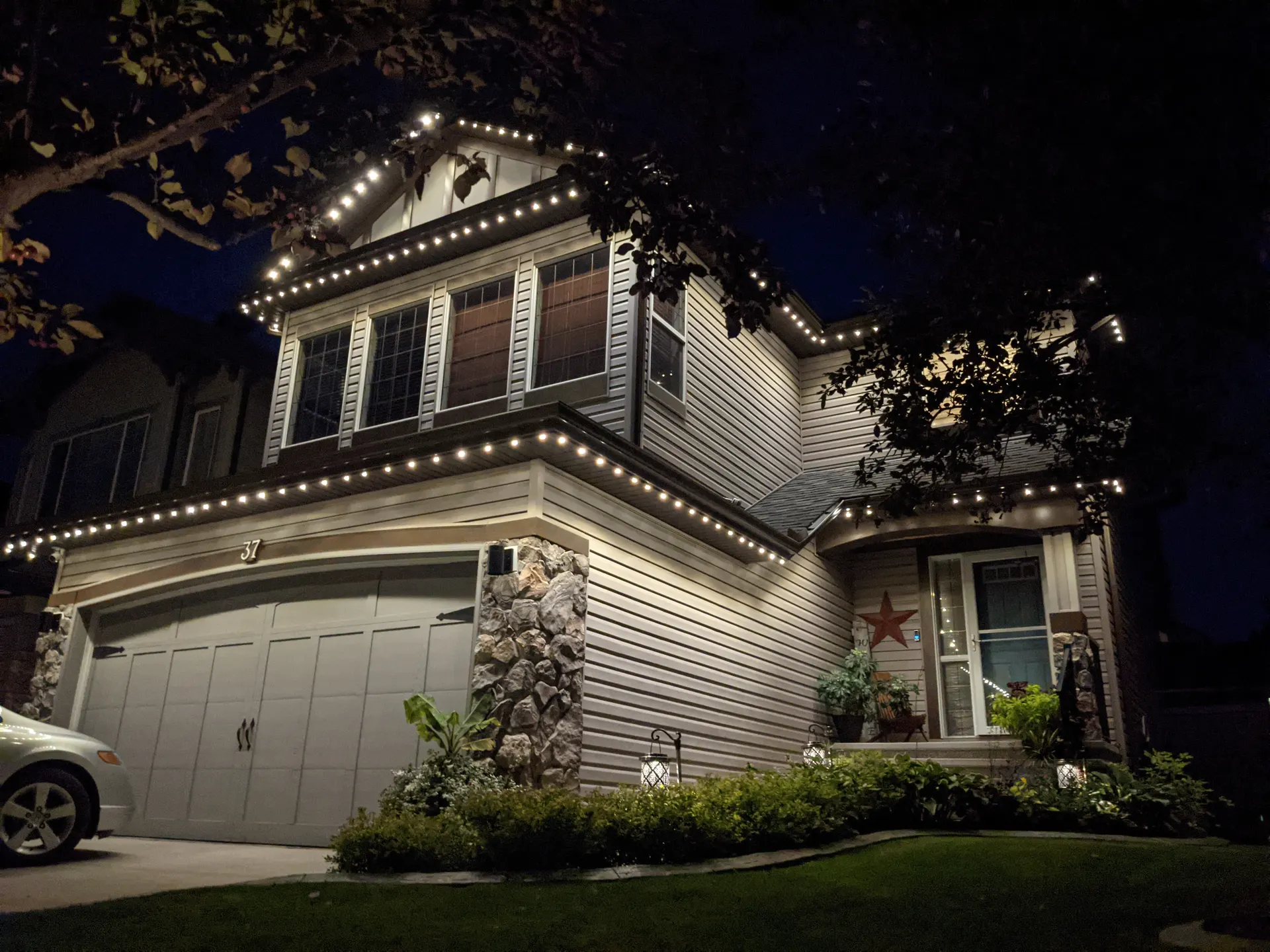 Two-story home outlined warm white, eaves peaks porch, tree-framed night
