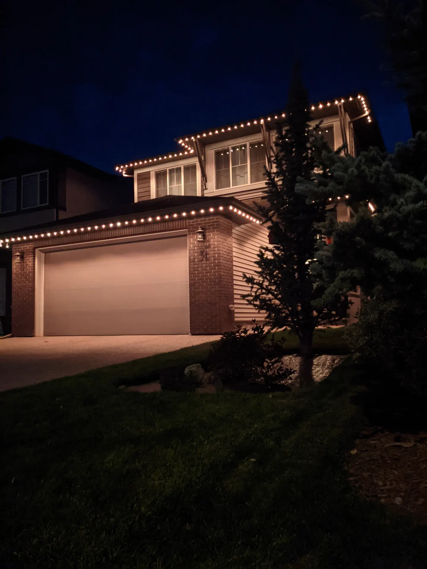 Two-story home eaves and gables traced in crisp warm white at dusk