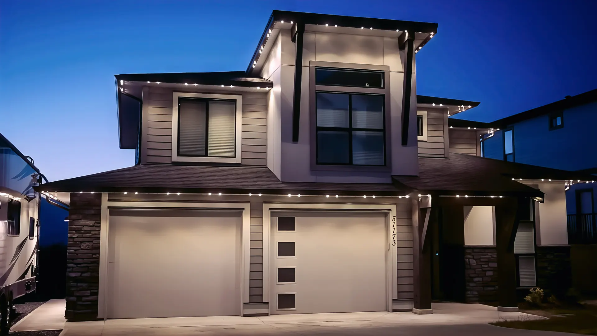 Modern two-story home eaves and peaks crisply outlined in warm white at dusk